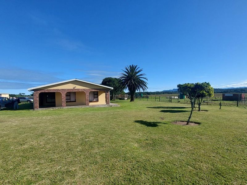 A single-story farmhouse featuring a covered patio with brick archways, set on a large, open grassy plot with perimeter fencing.