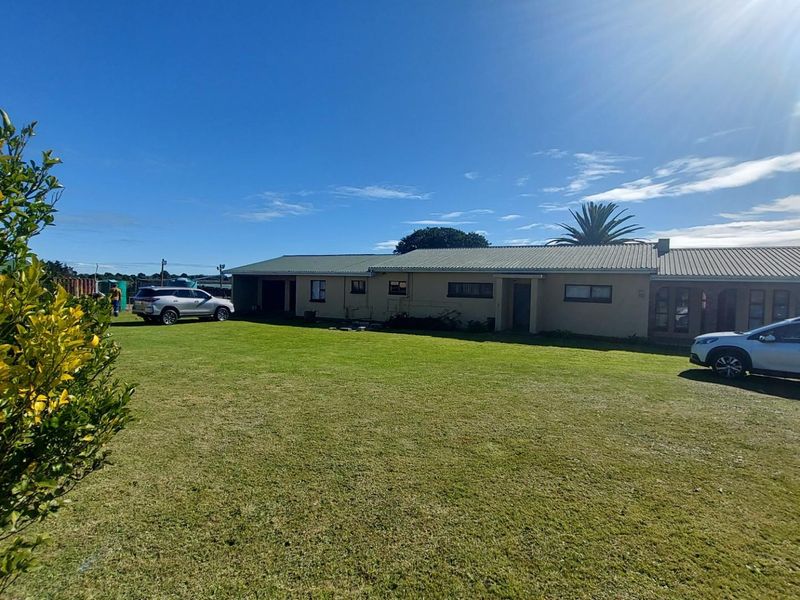 A wide-angle view of the rear exterior of the farm property, featuring a large lawn, plastered masonry walls, and a corrugated metal roof.