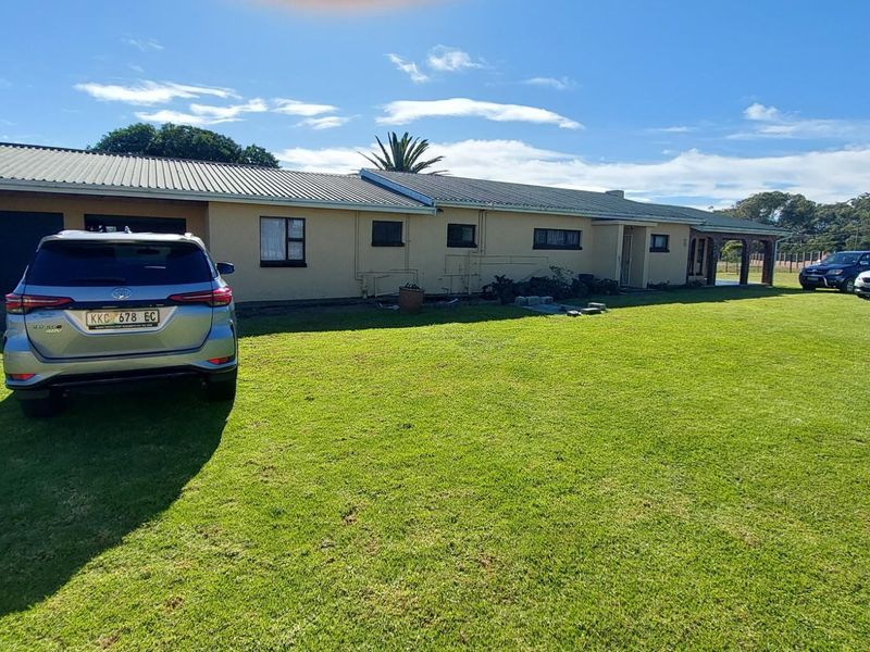 Rear view of a single-story farm house featuring a corrugated metal roof, attached garage, and a spacious lawn area.