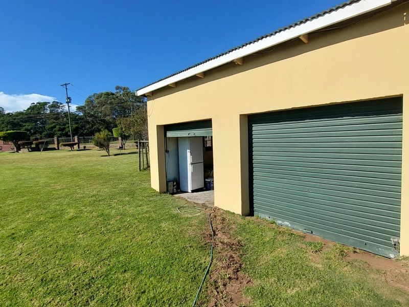 A detached garage structure with a roller shutter door, situated on a large open lawn area.