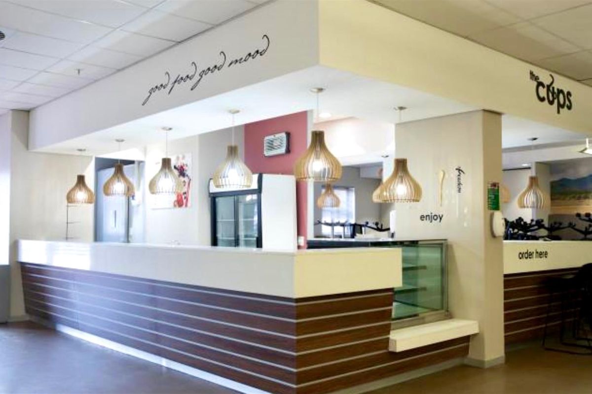 A commercial service counter area featuring a modern reception desk, integrated display refrigeration, and decorative pendant lighting in a clean, professional setting.