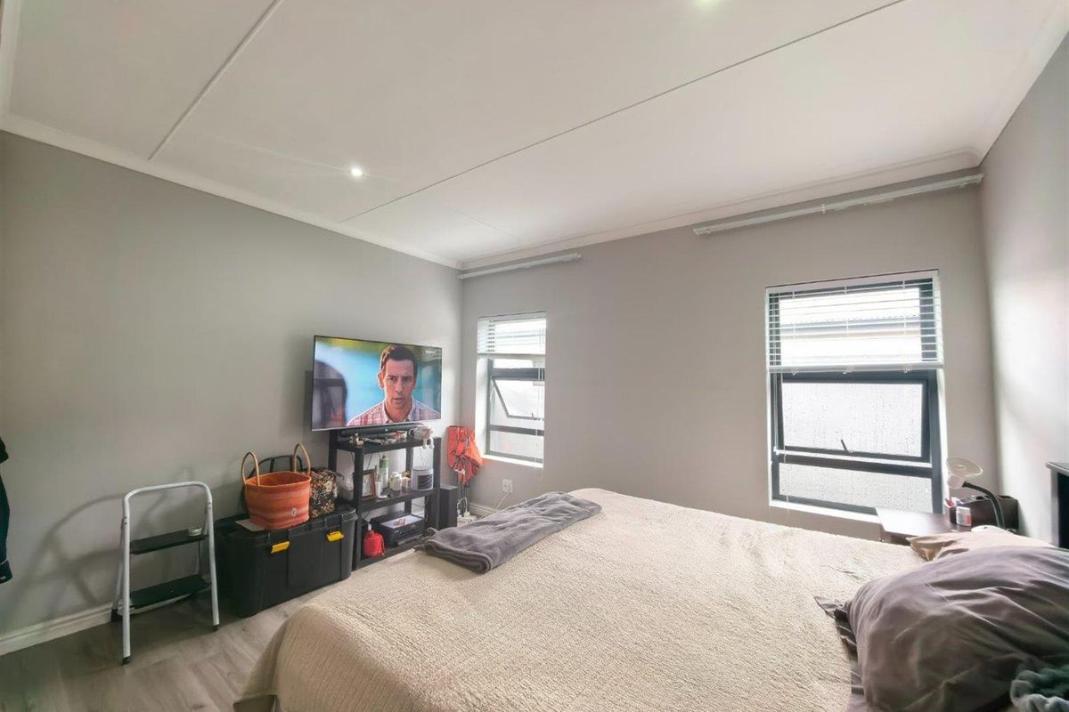 A well-maintained bedroom featuring neutral grey walls, modern laminate flooring, recessed downlighting, and aluminium-framed windows with fitted venetian blinds.