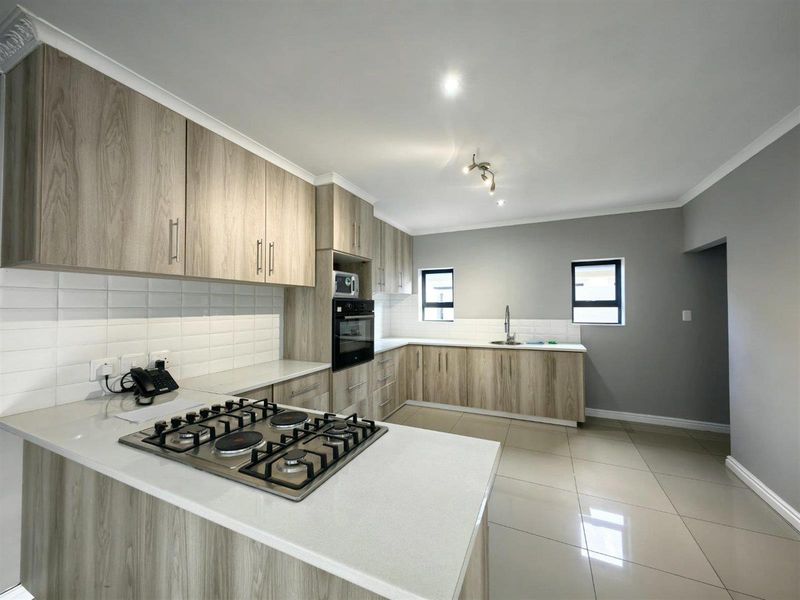 Modern kitchen featuring light wood-grain cabinetry, quartz countertops, a gas hob, built-in oven, and a clean subway tile backsplash.