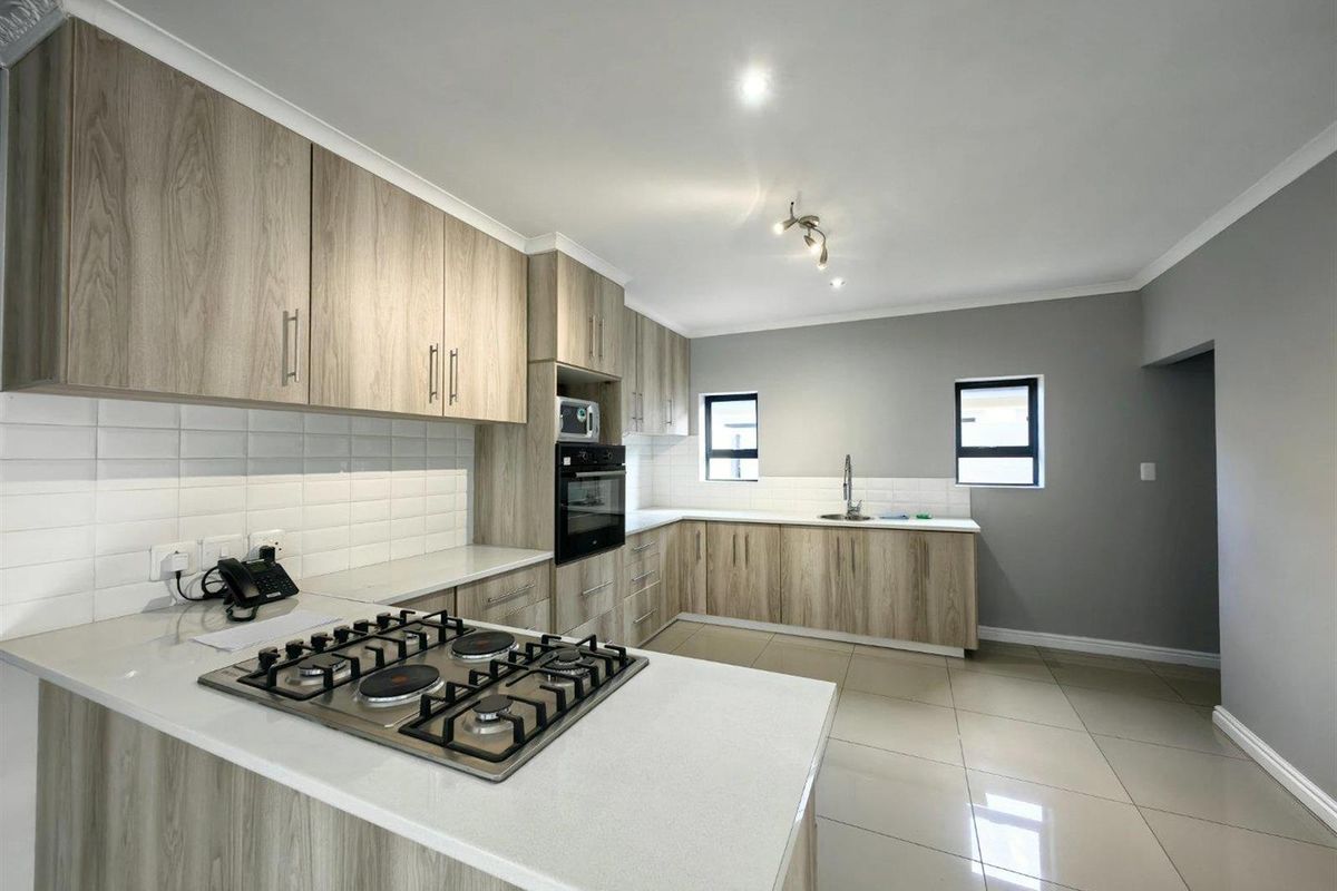 Modern kitchen featuring light wood-grain cabinetry, quartz countertops, a gas hob, built-in oven, and a clean subway tile backsplash.