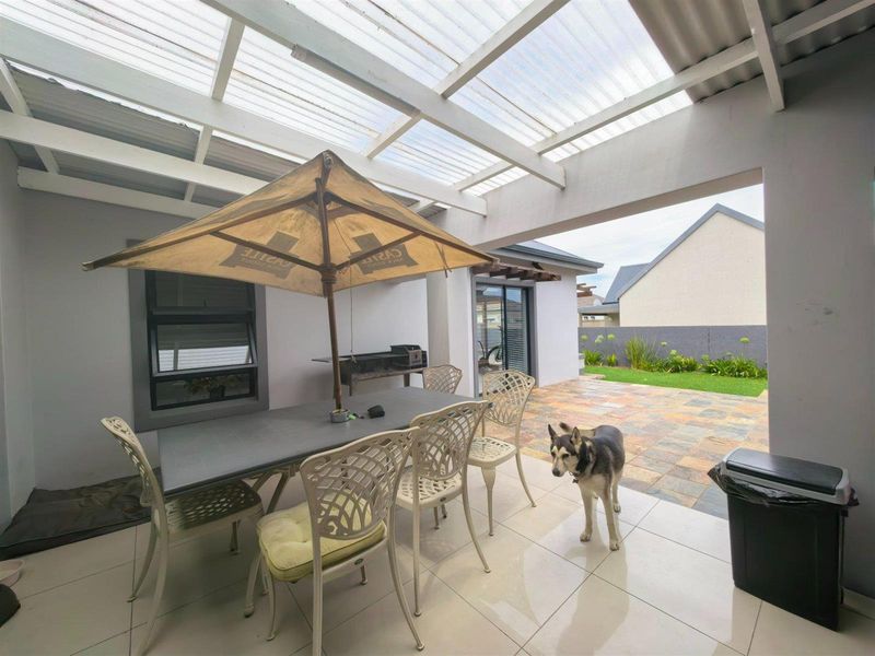 Covered patio area featuring tiled flooring, a translucent roof structure, and a built-in braai, providing a functional outdoor entertainment space.