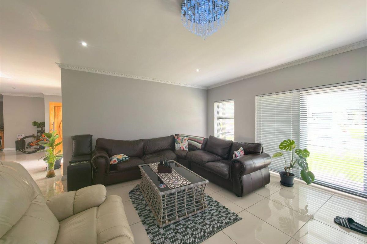 Spacious living room featuring polished tiled flooring, decorative ceiling cornice, recessed lighting, and large sliding glass doors with venetian blinds for natural light.