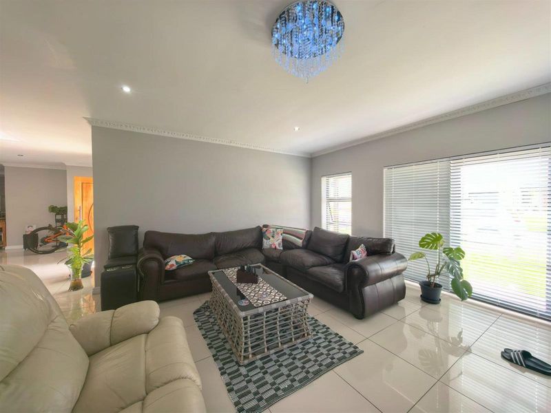 Spacious living room featuring polished tiled flooring, decorative ceiling cornice, recessed lighting, and large sliding glass doors with venetian blinds for natural light.