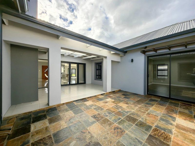 A spacious covered patio featuring natural slate tile flooring, modern sliding glass doors, and a pergola, offering a seamless transition to the interior living space.