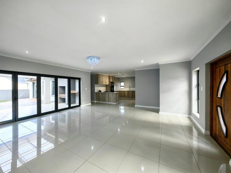 Spacious open-plan living area featuring polished porcelain tiles, modern kitchen with built-in appliances, and large aluminium stacker doors leading to the patio.
