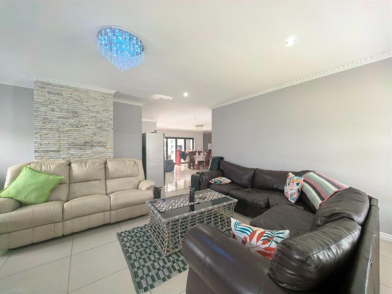 Spacious open-plan living area featuring a stone accent wall, decorative ceiling cornices, recessed lighting, and neutral tiled flooring throughout.