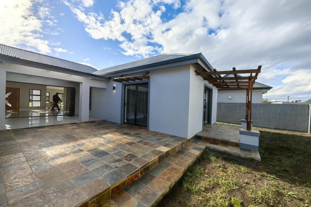 Rear exterior view featuring a spacious slate-tiled patio, timber pergola, and sliding glass doors leading into the main living area.