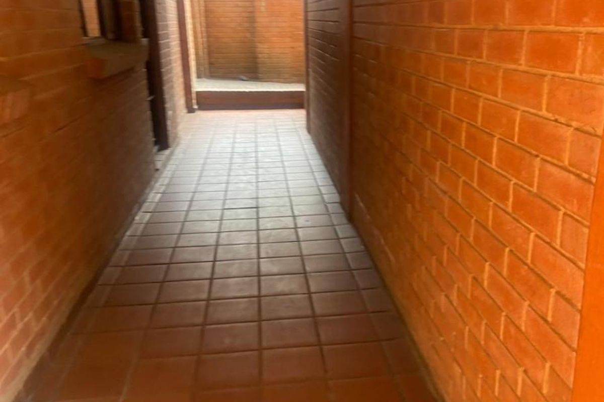 A narrow outdoor walkway or corridor featuring exposed brick walls and tiled flooring, providing access to the rear area of the property.