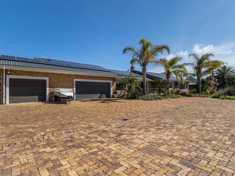 Front view of the property featuring a spacious paved driveway, double garage, and extensive roof-mounted solar panel installation.