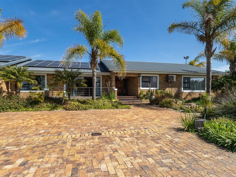 Front elevation of a brick-faced small holding featuring a paved driveway, solar panel installation, and established garden landscaping.