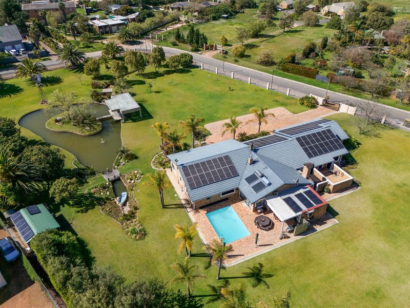 Aerial view of a small holding property featuring a main residence with solar panels, a swimming pool, a landscaped garden, and a private pond.
