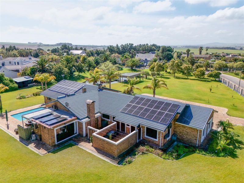 Aerial view of a spacious small holding property featuring a brick residence with solar panels, a swimming pool, and extensive landscaped grounds.