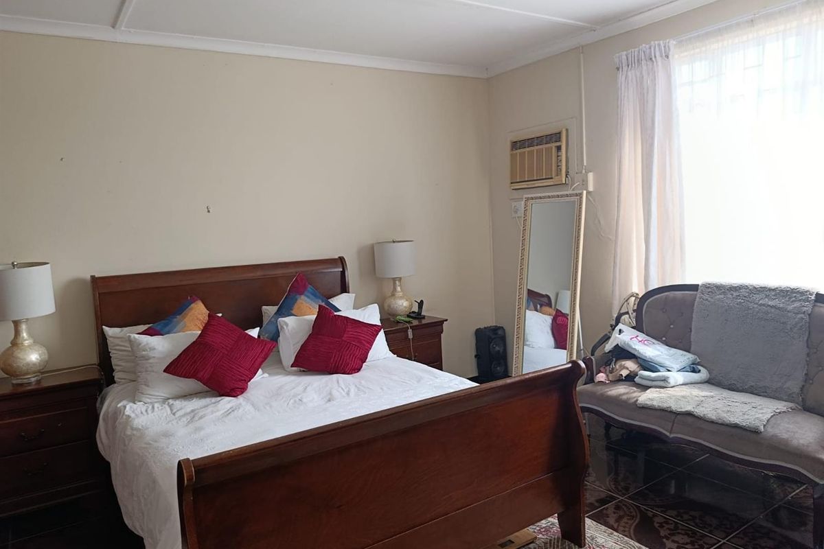 A bedroom featuring a built-in window air conditioning unit, tiled flooring, and large windows with curtains.