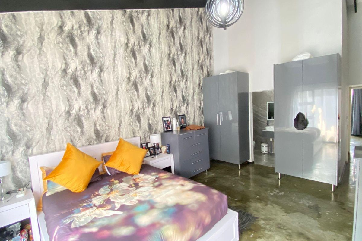Spacious bedroom featuring high ceilings, a feature wallpaper wall, polished concrete flooring, and an en-suite bathroom.
