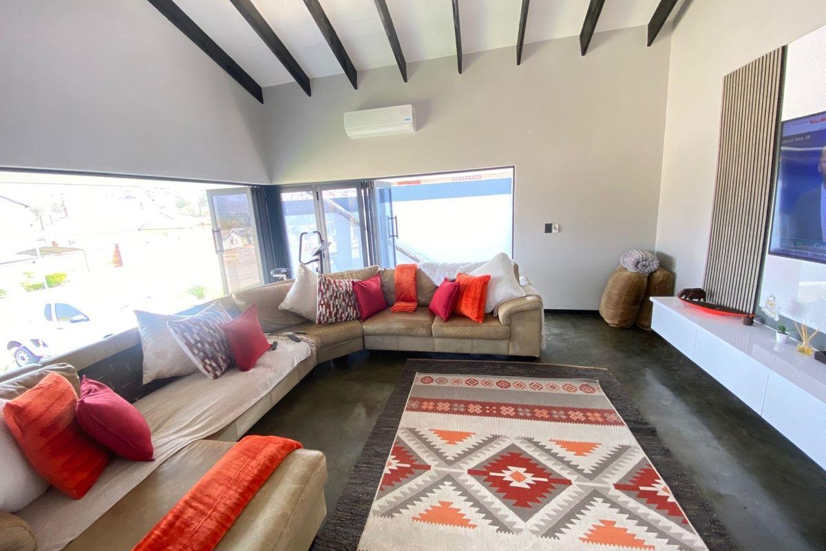 Spacious living room featuring high vaulted ceilings with exposed timber beams, polished concrete flooring, and large folding glass doors leading to the exterior.