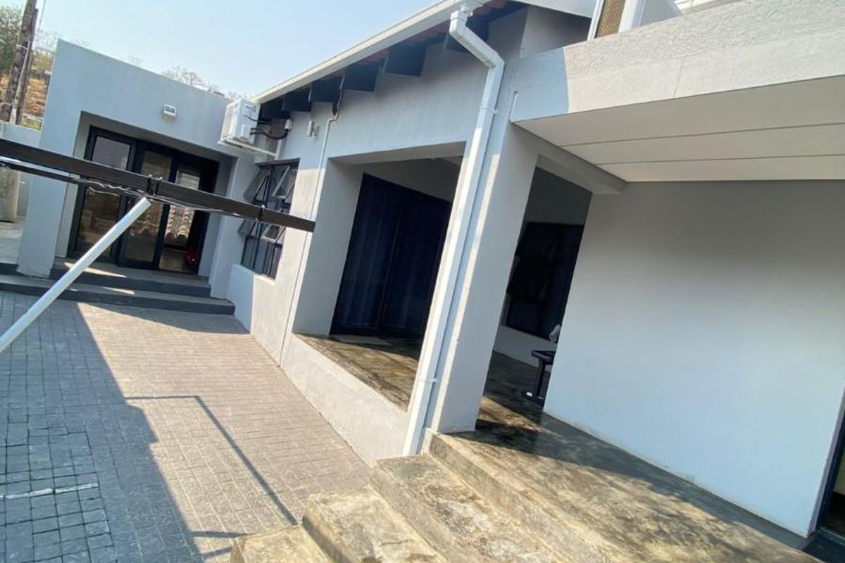 A rear exterior view of the house featuring a paved patio area, concrete steps, and modern grey exterior wall finishes.