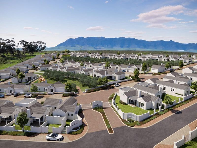 Aerial view of a modern residential estate featuring uniform white houses, paved streets, and landscaped grounds set against a mountain backdrop.