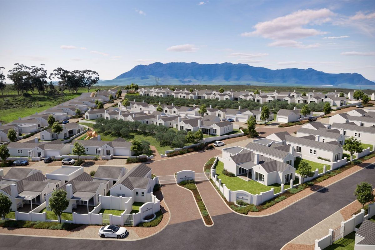 Aerial view of a modern residential estate featuring uniform white houses, paved streets, and landscaped grounds set against a mountain backdrop.