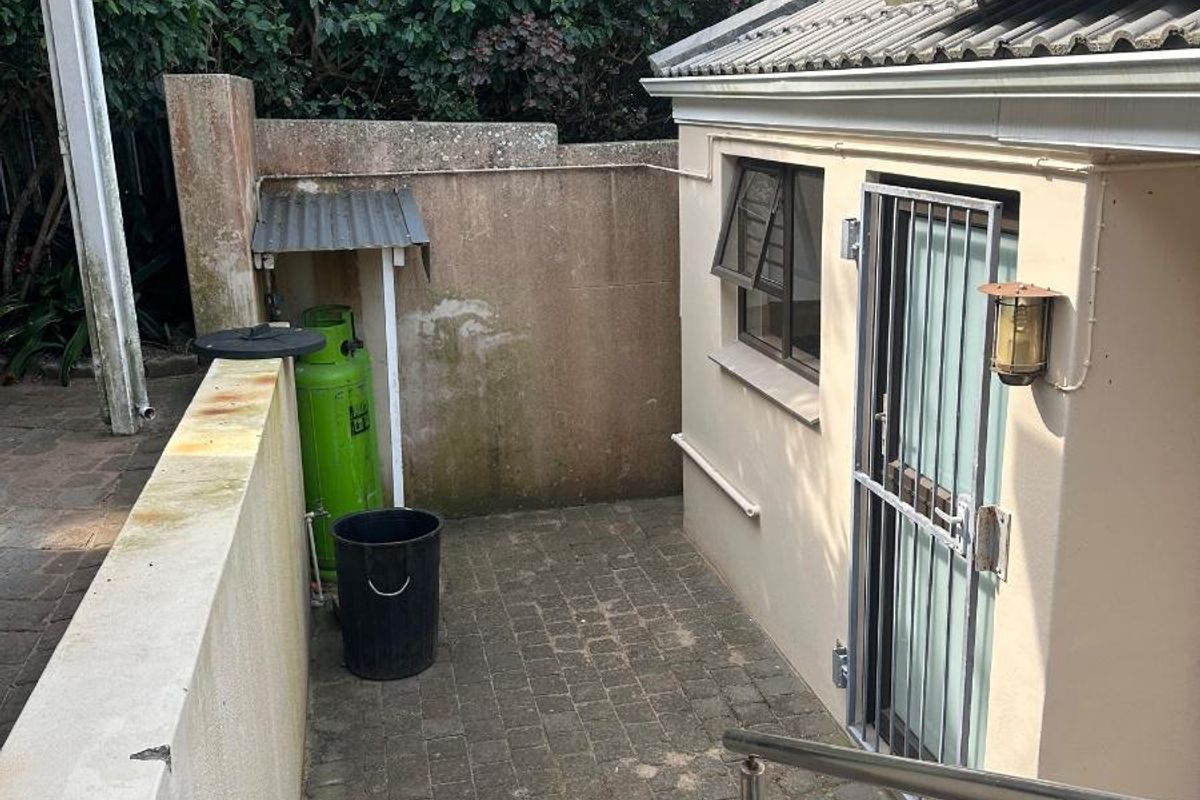 A paved side courtyard area featuring a security gate, stainless steel handrail, and solar panels mounted on the roof.