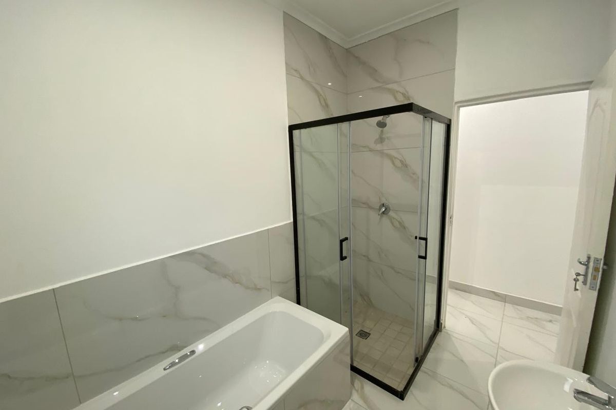 Modern bathroom featuring a sleek glass-enclosed shower, a contemporary bathtub, and elegant marble-look floor and wall tiling.