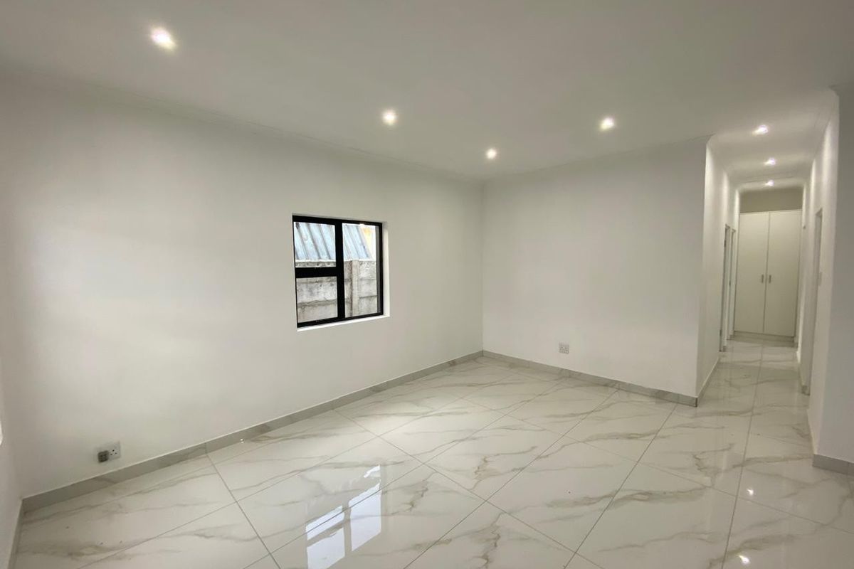 A bright, empty living area featuring modern marble-look floor tiles, recessed ceiling lighting, and a hallway leading to built-in storage cupboards.