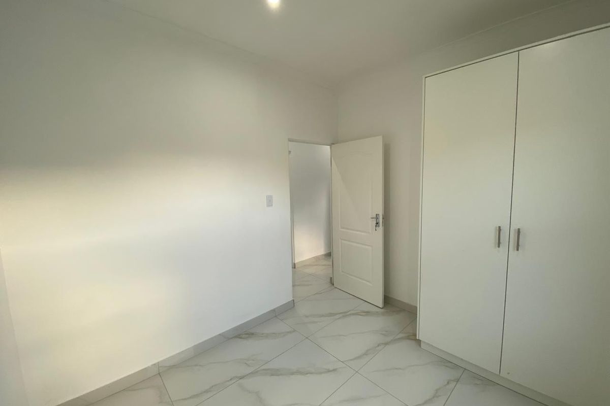 A clean, minimalist bedroom featuring neutral marble-look floor tiles and a built-in white wardrobe, offering a bright and modern living space.