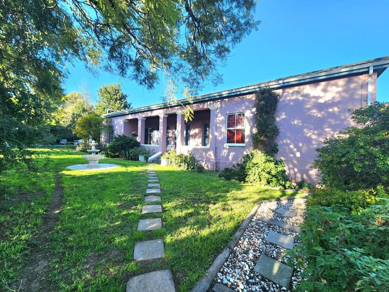 A view of the rear elevation featuring a covered patio, stone pathways, a decorative fountain, and a well-maintained garden area.