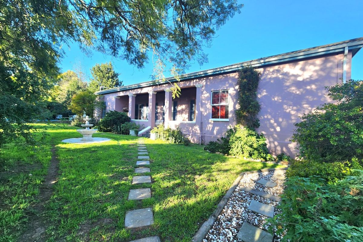 A view of the rear elevation featuring a covered patio, stone pathways, a decorative fountain, and a well-maintained garden area.