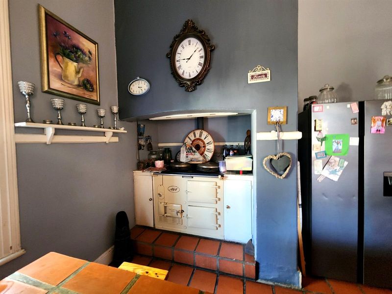 A kitchen featuring a classic Aga range cooker set within a tiled alcove, complemented by terracotta flooring and a neutral wall finish.