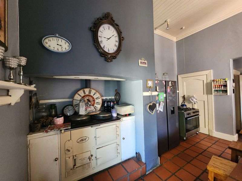 A rustic kitchen featuring a classic AGA range cooker, terracotta floor tiles, and high ceilings, offering a traditional and characterful cooking space.