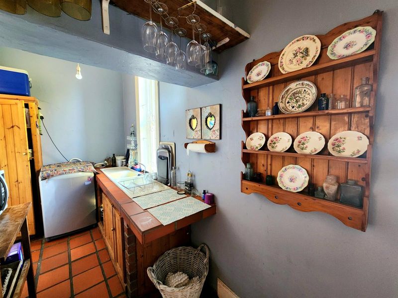 A functional scullery area featuring terracotta floor tiles, a double basin sink with tiled countertop, and built-in wooden cabinetry.