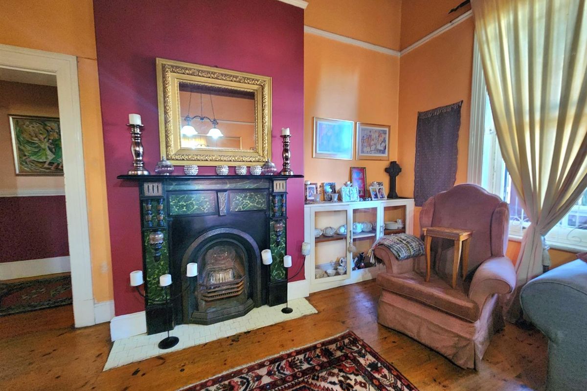A living room featuring a characterful ornate fireplace, polished timber flooring, and built-in shelving, set within a space with high ceilings.