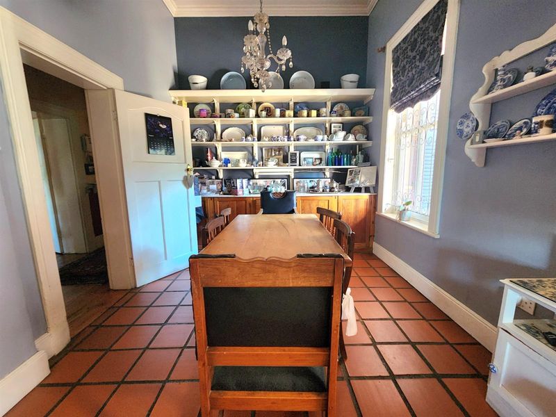 A dining room featuring terracotta floor tiles, built-in display shelving, and a classic chandelier, offering a traditional aesthetic with potential for modern updates.