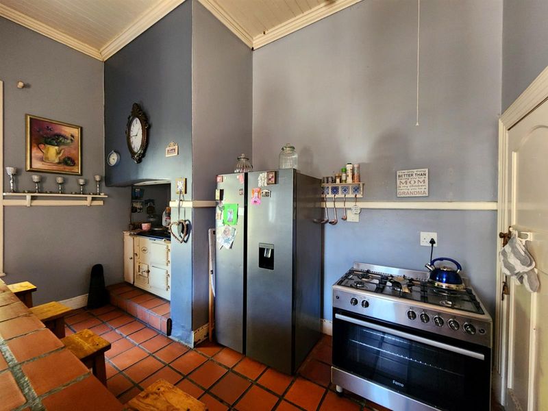 A rustic kitchen featuring terracotta tile flooring, a vintage range cooker, and a modern gas stove, set against high ceilings with classic architectural details.