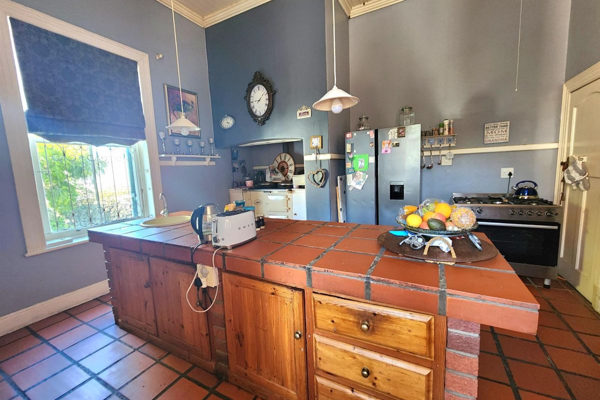A rustic kitchen featuring a large tiled island, wooden cabinetry, gas stove, and terracotta floor tiles, offering a traditional and functional cooking space.