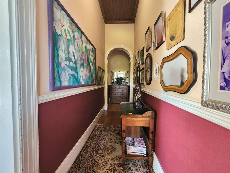 A traditional hallway featuring a timber-paneled ceiling, decorative archway, and classic dado rail detailing with hardwood flooring.