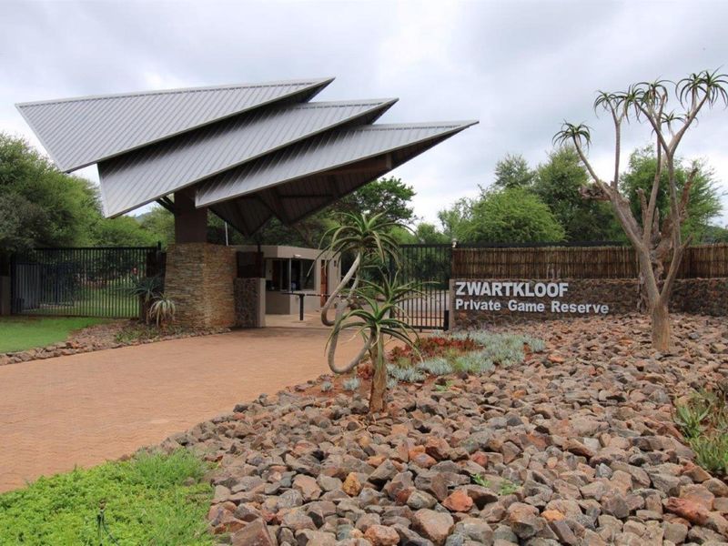 The entrance gate to Zwartkloof Private Game Reserve, featuring a modern architectural roof structure, stone masonry, and secure gated access.