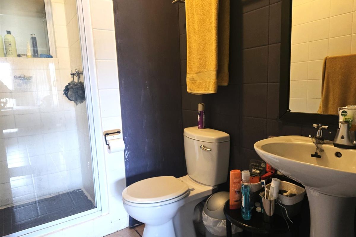 A functional bathroom featuring a shower enclosure, pedestal basin, and toilet with dark tiled accent wall.