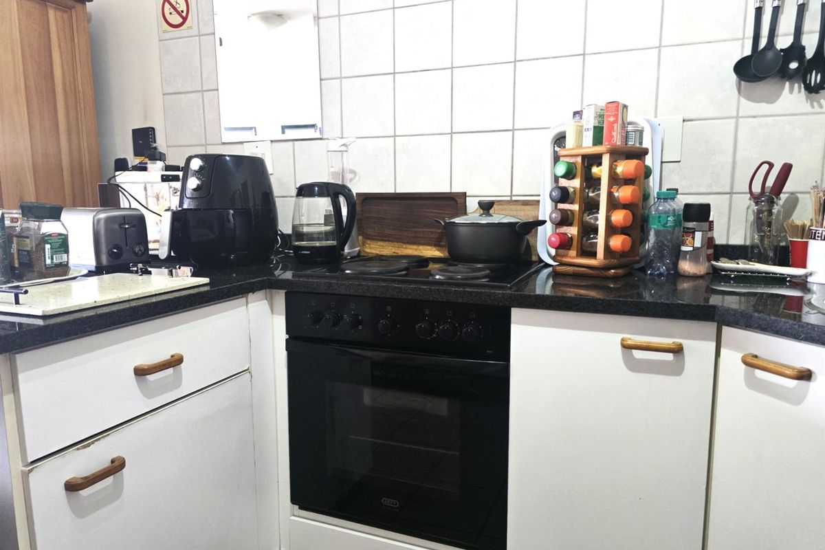 Compact kitchen featuring white cabinetry, dark granite countertops, and a built-in electric oven with a ceramic hob.