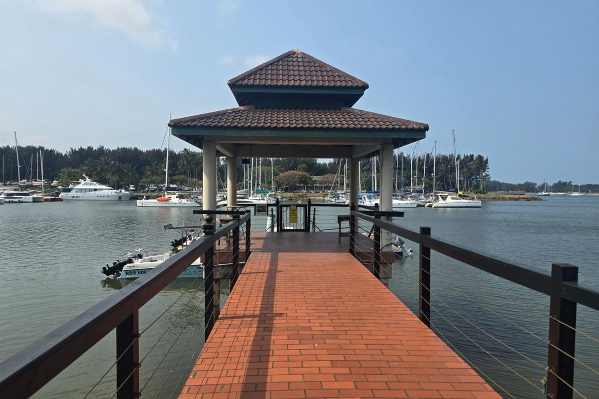A scenic wooden pier with a covered gazebo structure extending over the water, offering views of the marina and docked boats.