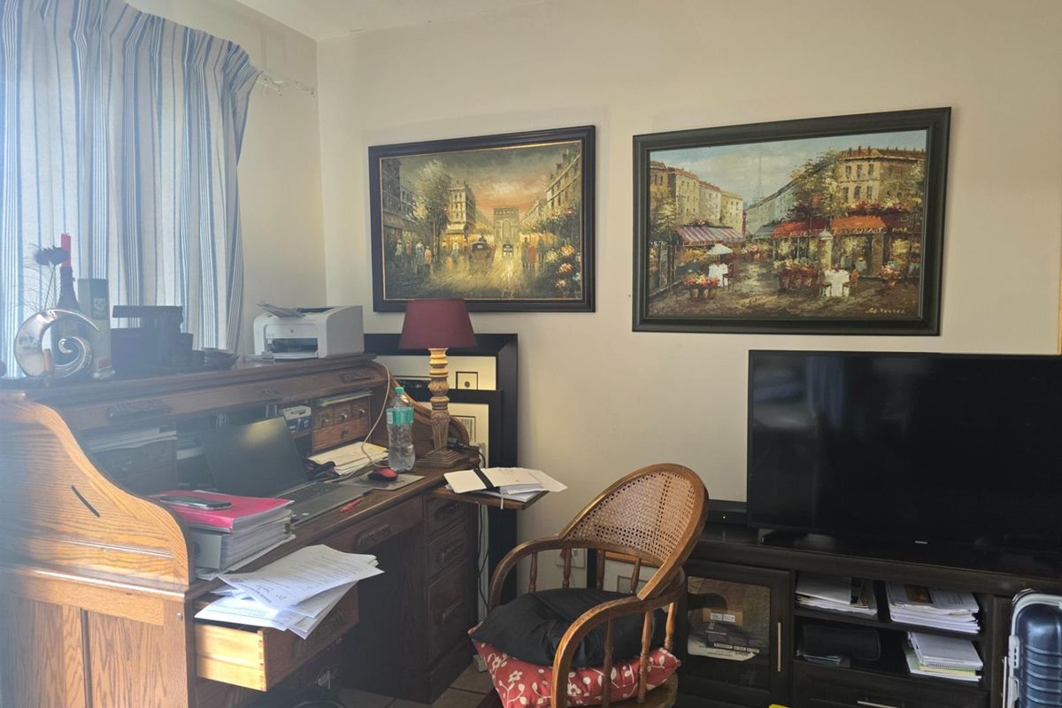 A living room area featuring tiled flooring and window treatments, currently utilized as a home office and media space.