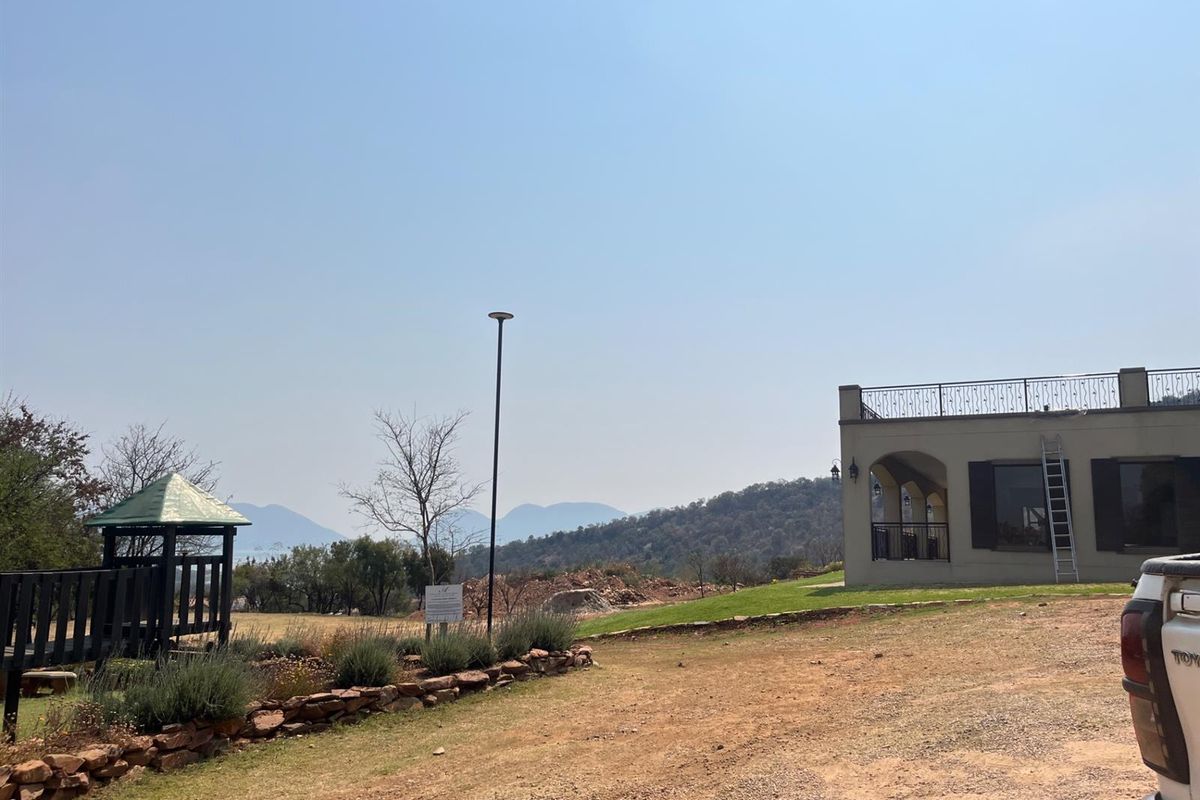 Exterior view of a residential property featuring a landscaped garden, a small gazebo, and a building with a balcony overlooking scenic mountain views.