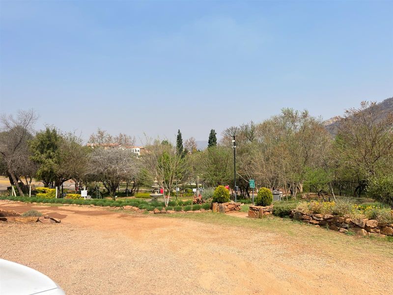 A view of a landscaped garden area featuring mature trees, stone retaining walls, and a gravel driveway on a residential property.