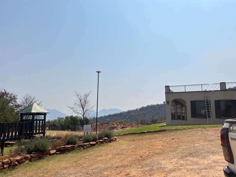Exterior view of a residential property featuring a landscaped garden, a small gazebo, and a building with a balcony overlooking scenic mountain views.