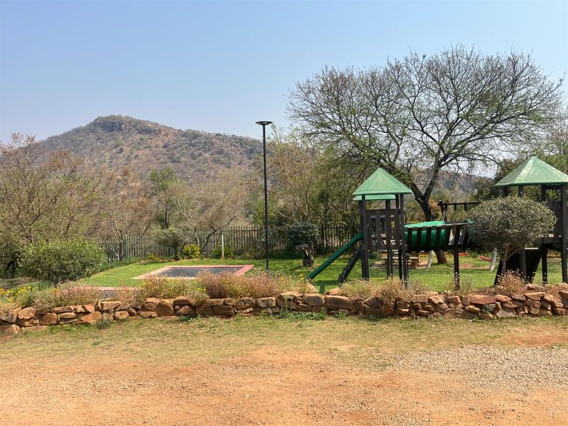 A landscaped garden area featuring a built-in playground structure, in-ground trampoline, stone retaining wall, and scenic mountain views.