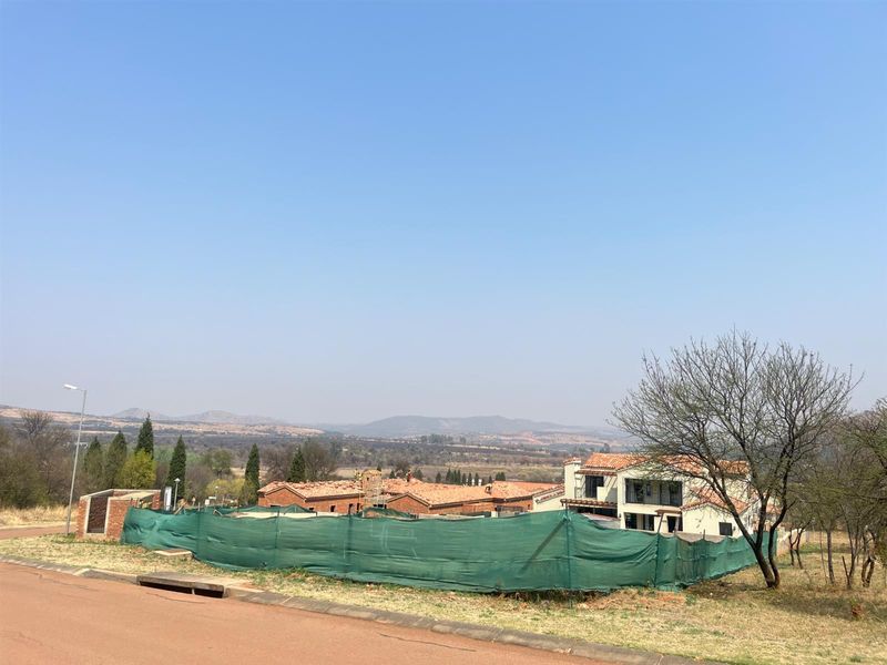 A view of a residential development site featuring ongoing construction, surrounded by natural landscape and distant mountain views.